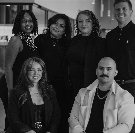 A group portrait of six professionally dressed people smiling at the camera, representing a diverse and collaborative team.